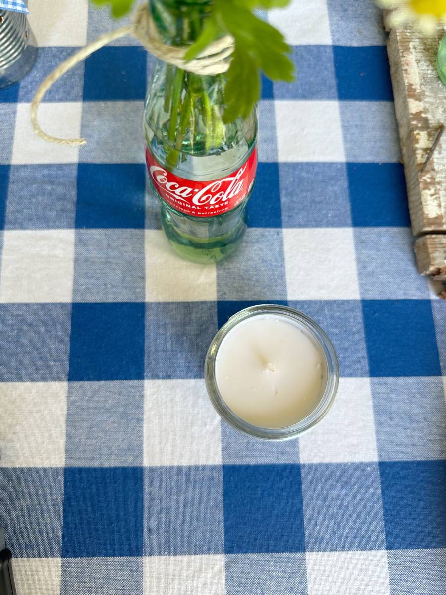 tea light candle in small mason jar beside flowers in coke bottle on blue and white check tablecloth