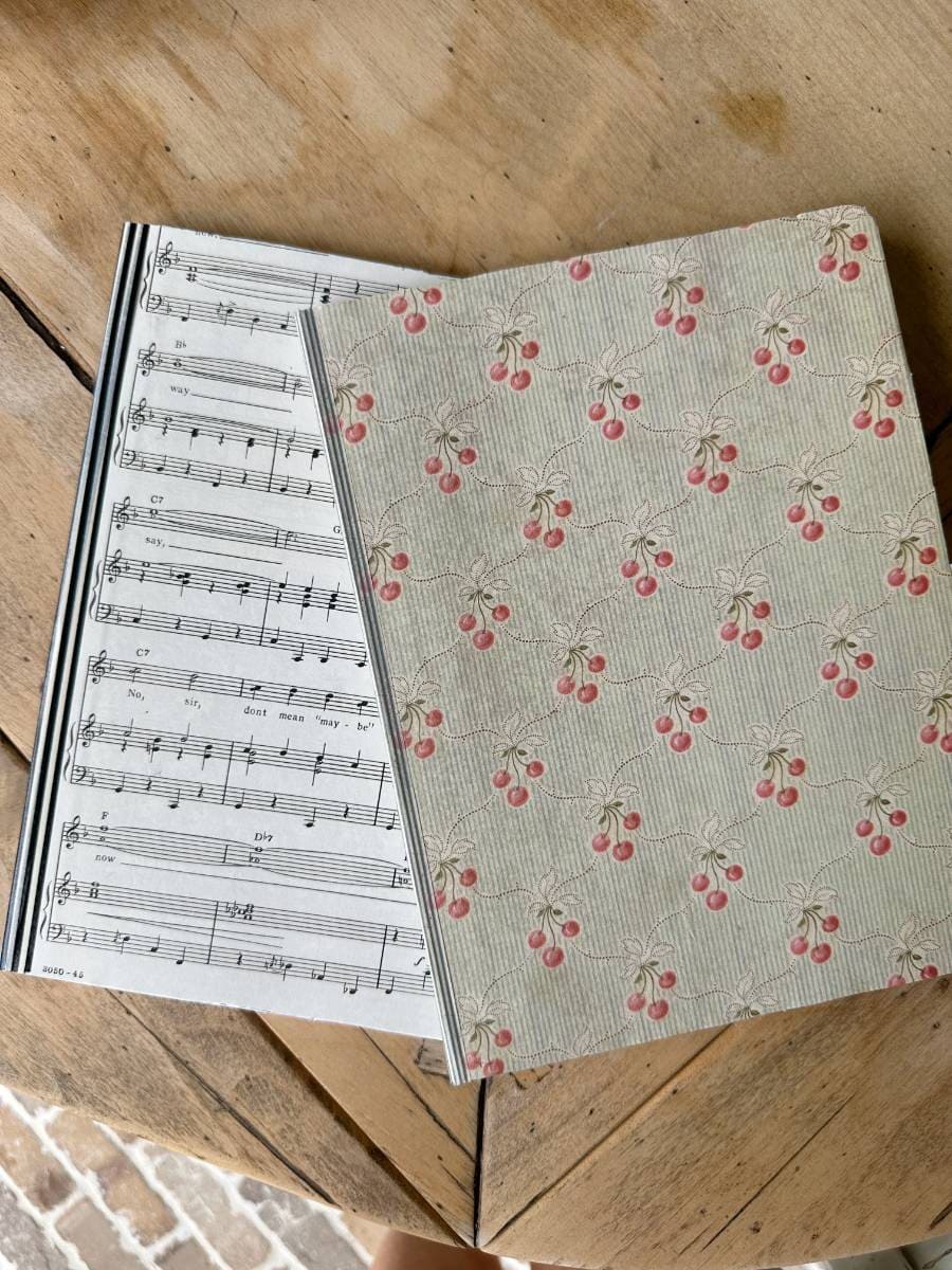 2 handmade journal notebooks with sheet music on cover and decorative paper on other and washi tape on binding