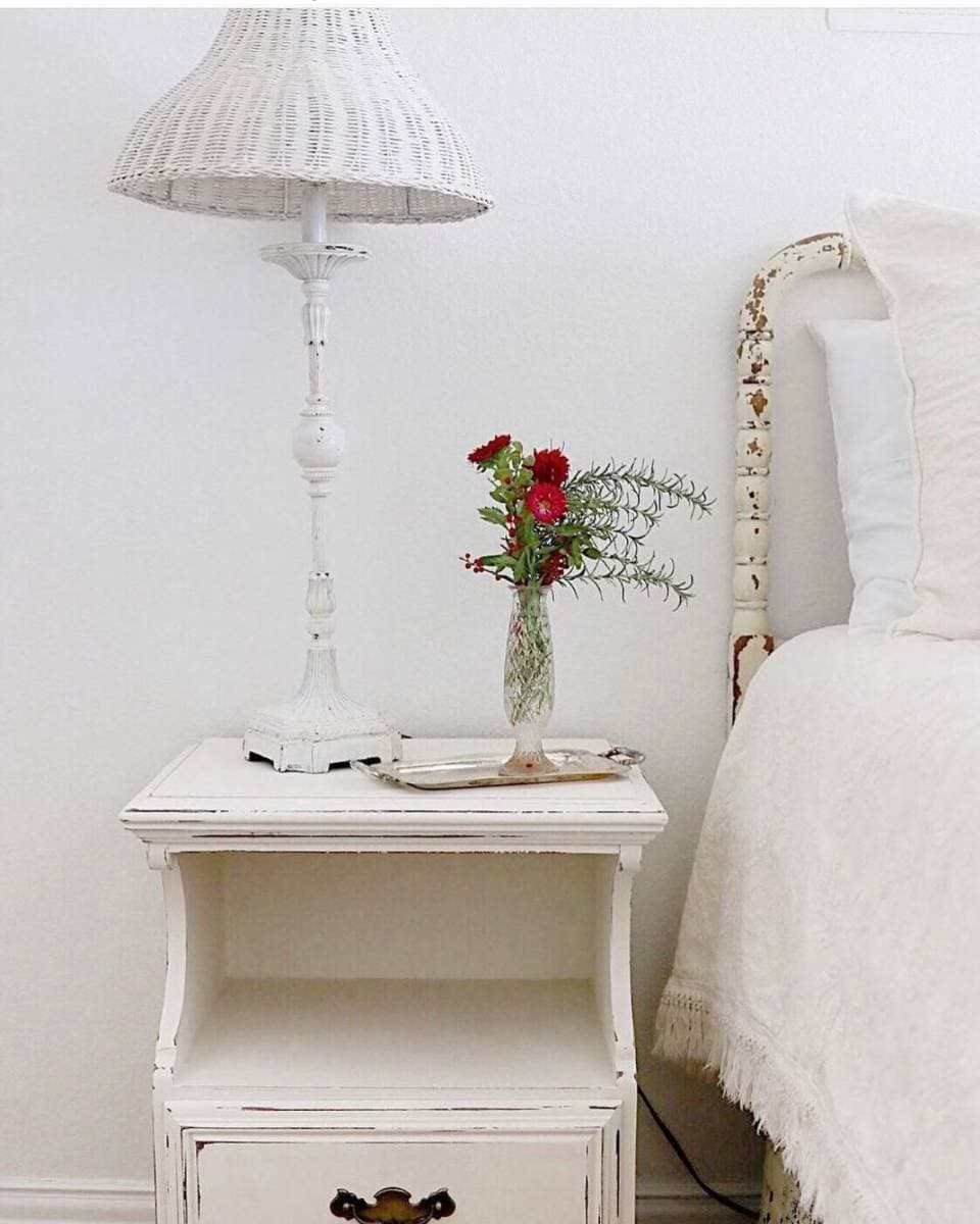 white nightstand with lamp and vase of flowers in guest bedroom
