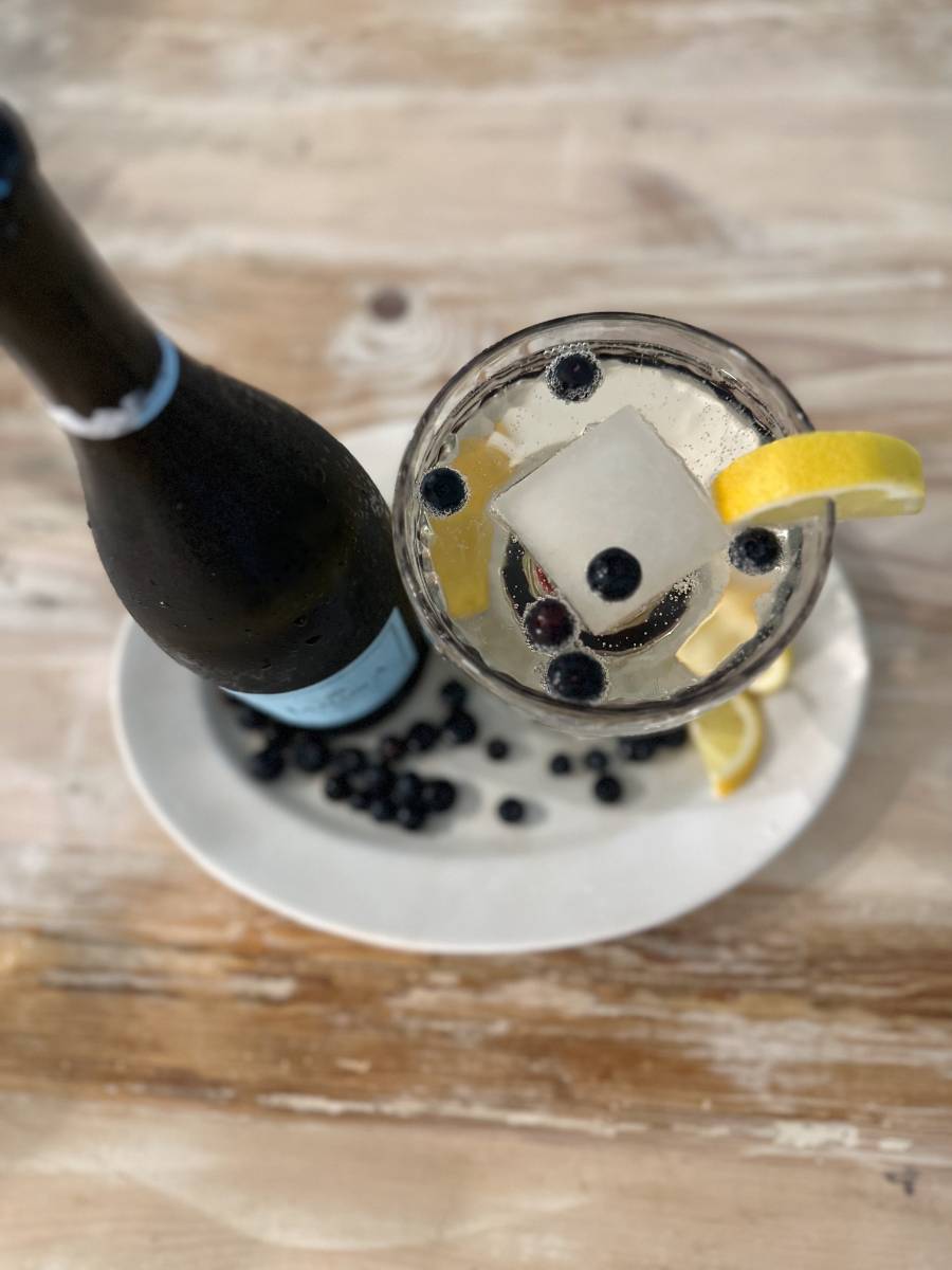 making a blueberry prosecco cocktail with bottle of prosecco lemon blueberries cocktail glass with lemonade ice cube