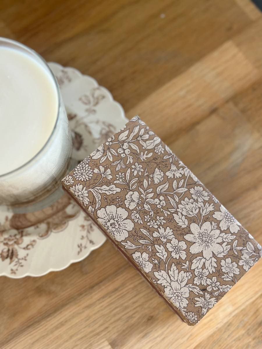 A glass of milk on a floral-patterned plate sits beside a decoupage decorated matchbox, showcasing intricate DIY artistry on the wooden table.